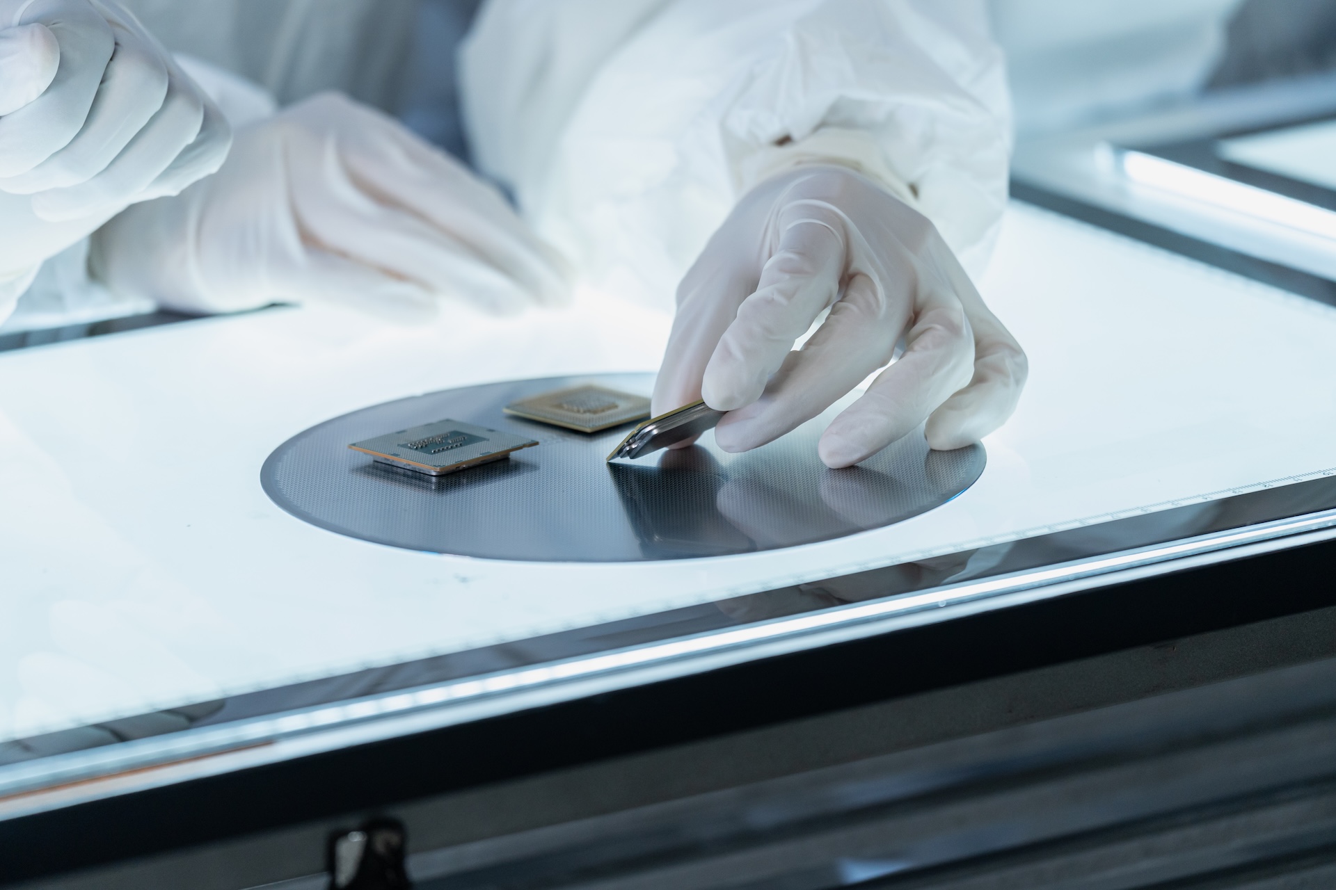 Avnan | 5 Engineering Factors That Influence Heat Pump Efficiency | Close-up of a technician's gloved hands carefully inspecting semiconductor microchips and a silicon wafer on an illuminated light table in a cleanroom laboratory